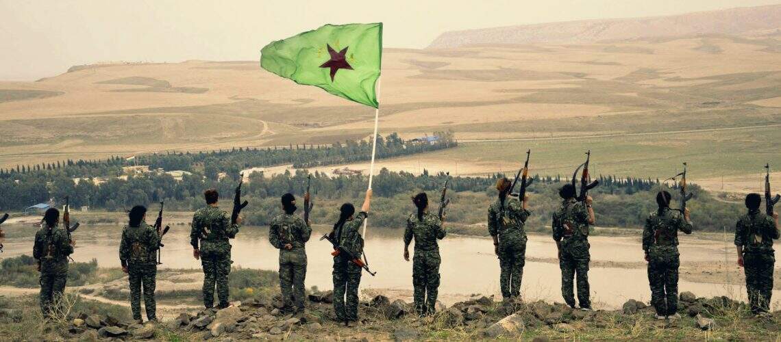 Fighters_of_the_YPJ_stand_atop_a_hill_with_their_flag